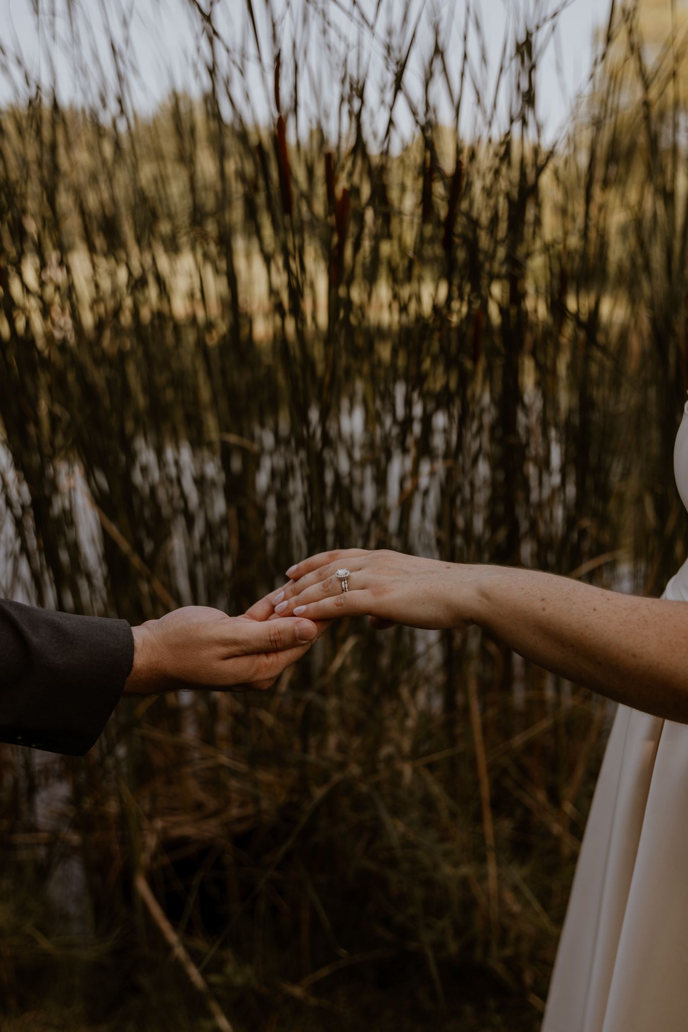 Close-up of hands reaching toward each other during an outdoor wedding ceremony.