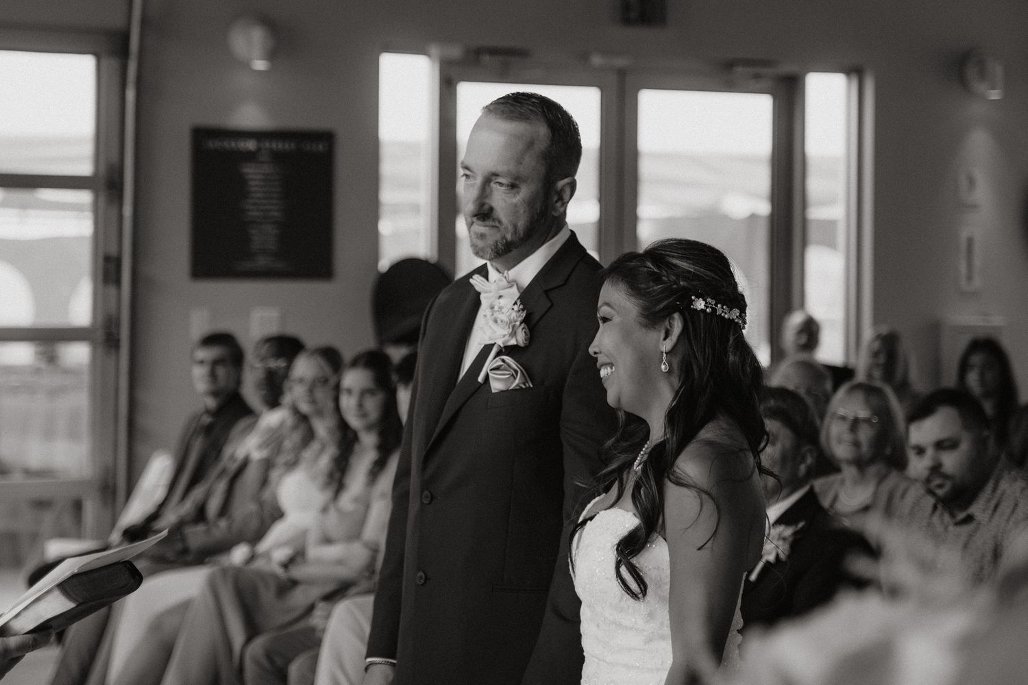 Wedding guests watch emotionally during a ceremony in a bright venue.