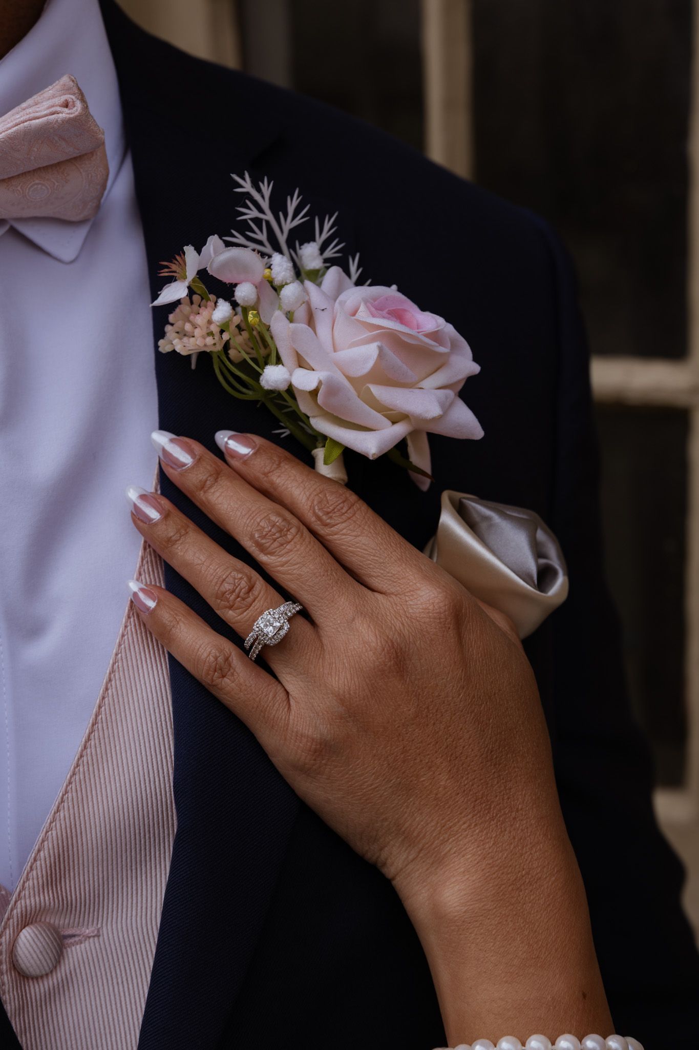 Close-up of pink rose boutonniere and wedding ring details on formal attire.