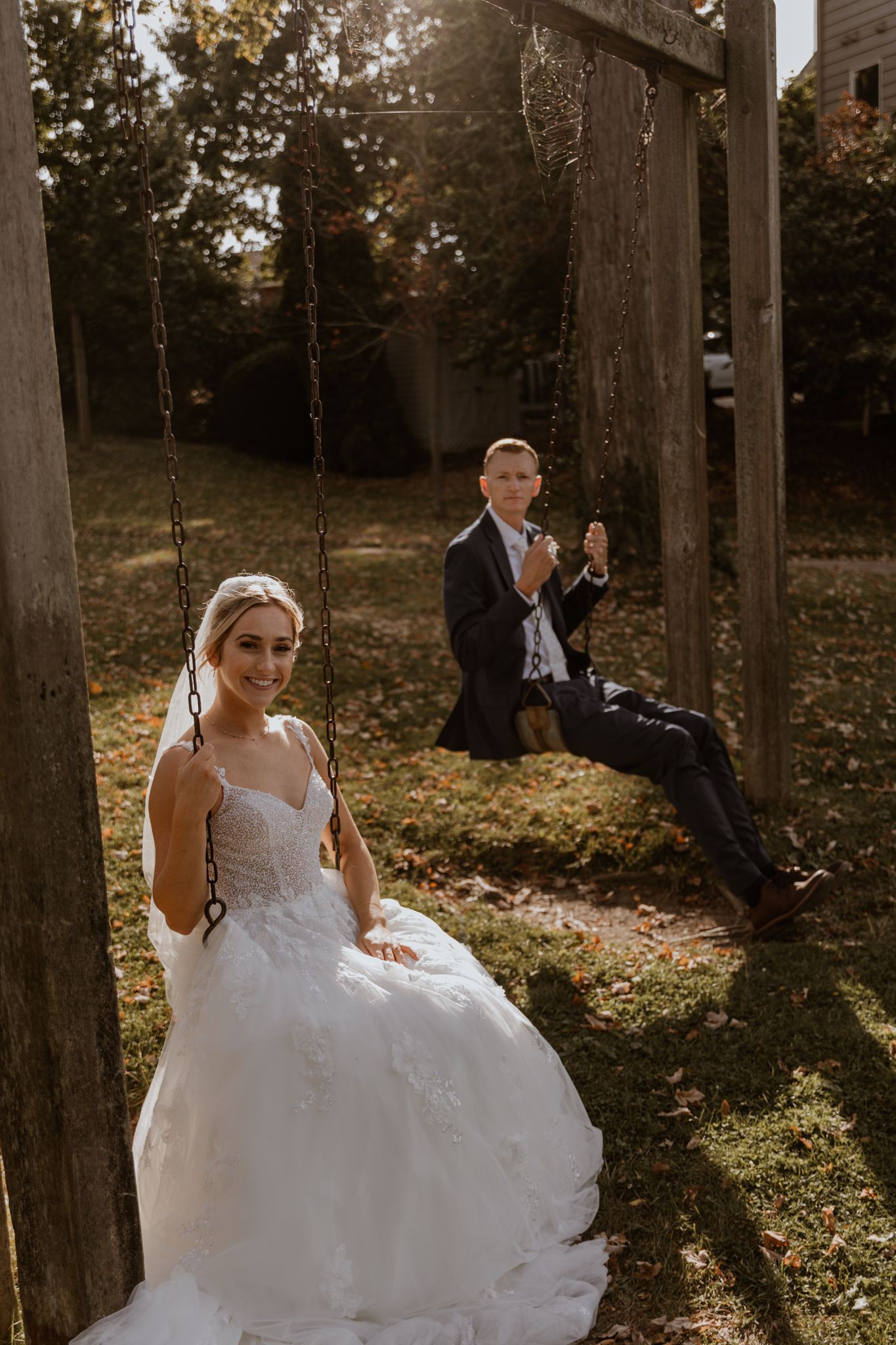 A wedding scene with a bride in white dress and groom on swing set in a garden setting.