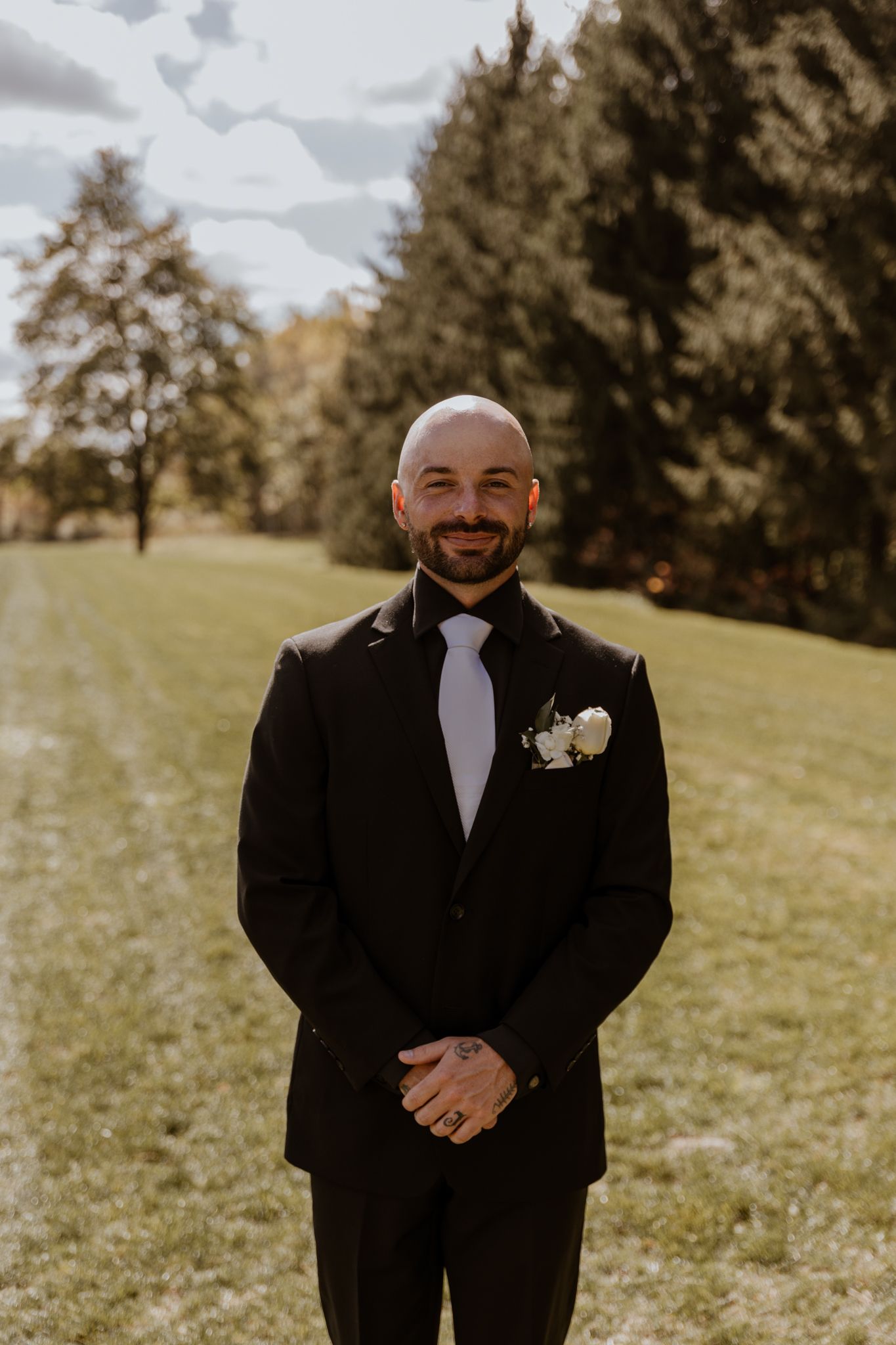A person in formal attire smiles joyfully during an outdoor wedding celebration.
