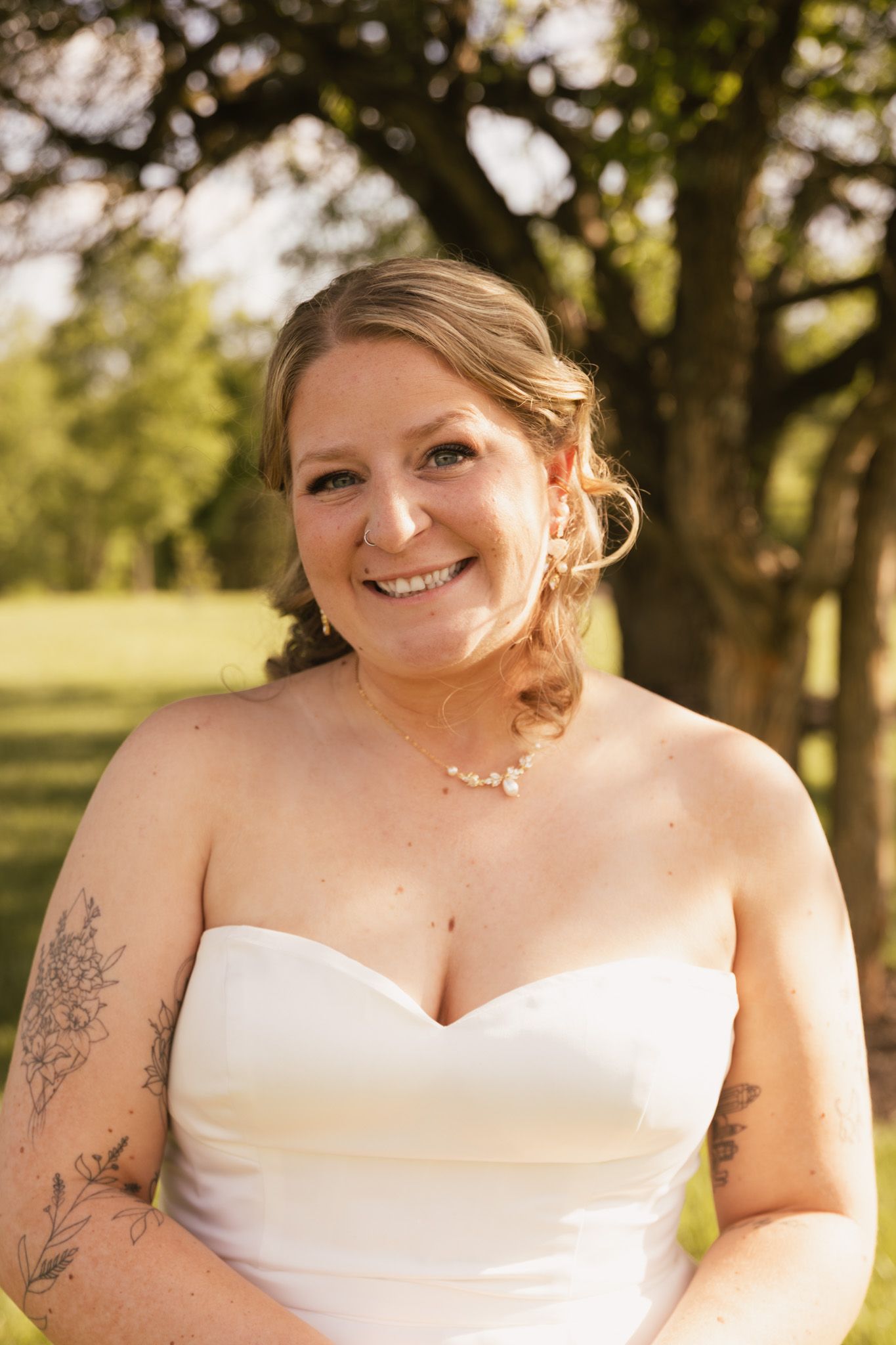 Bride in white strapless gown poses against natural outdoor backdrop.
