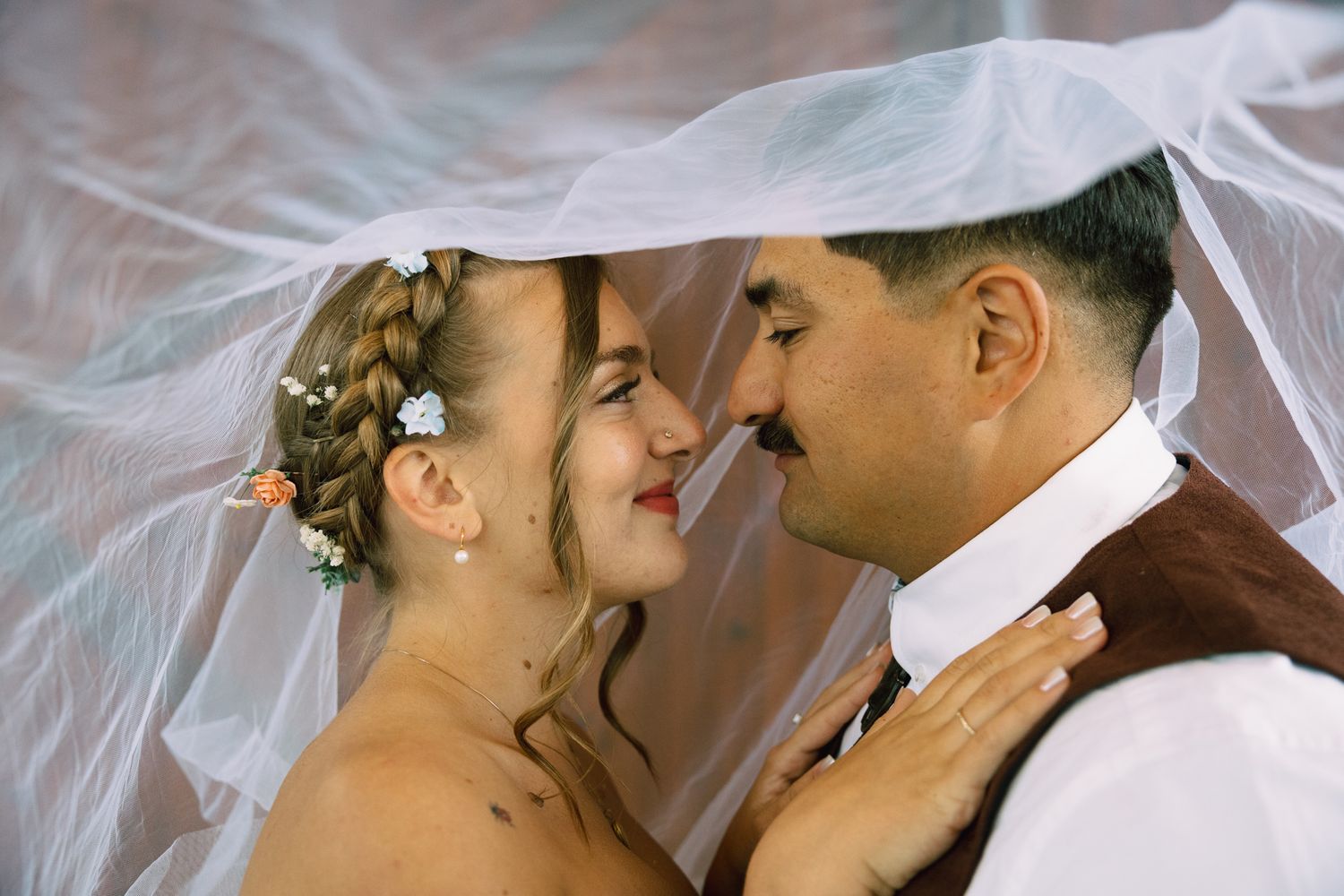 Bride and groom sharing a romantic moment under a flowing white veil on their wedding day.