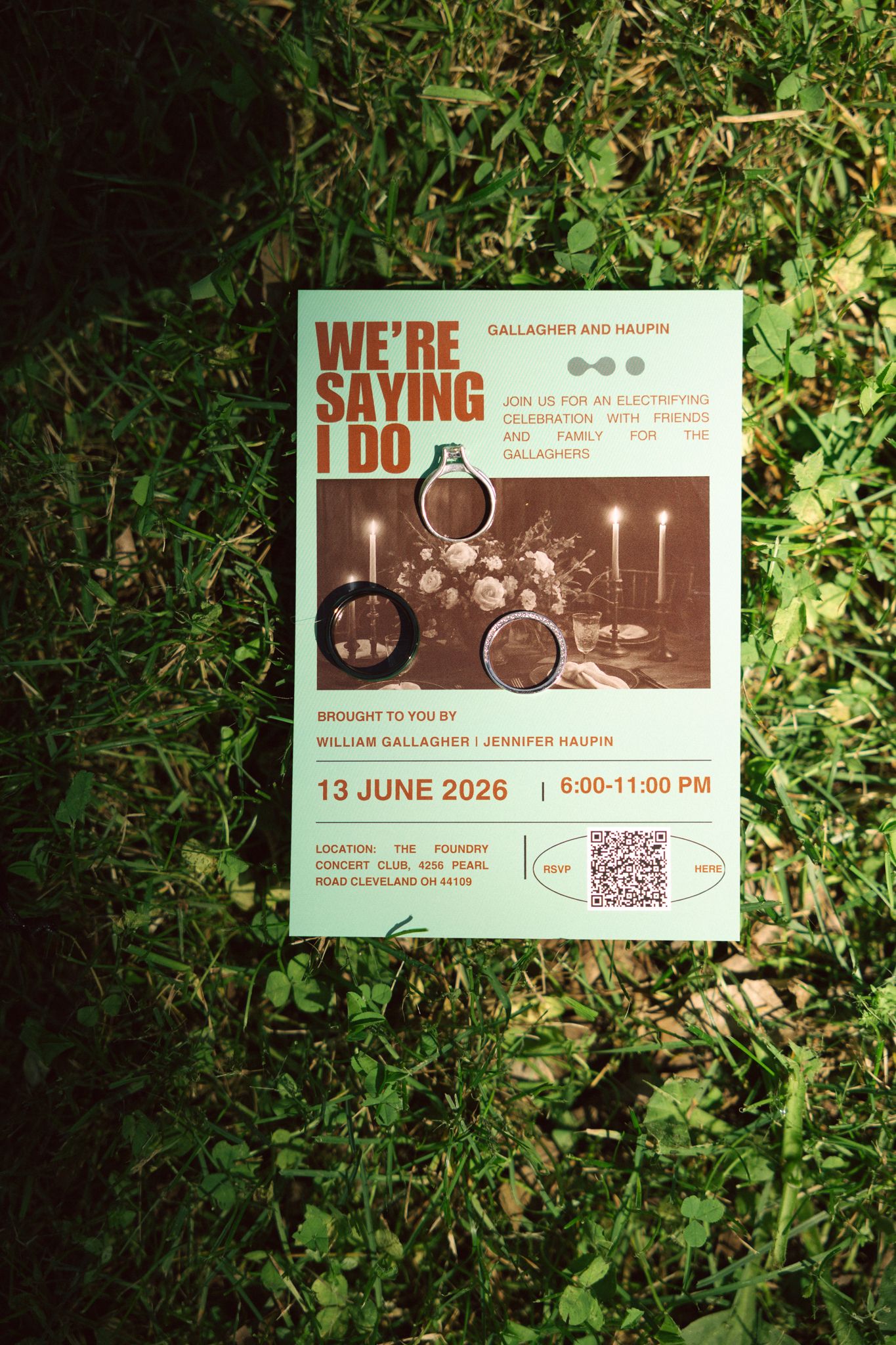 Wedding save-the-date card reading We're Saying I Do for Gallagher and Haupin on June 13 2026 laid on green grass.