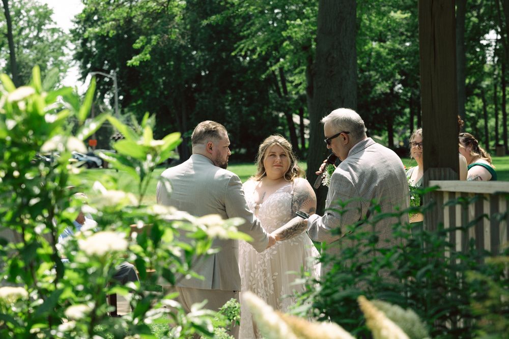 Bride and groom exchange vows outdoors in a lush garden ceremony with an officiant on a sunny day.