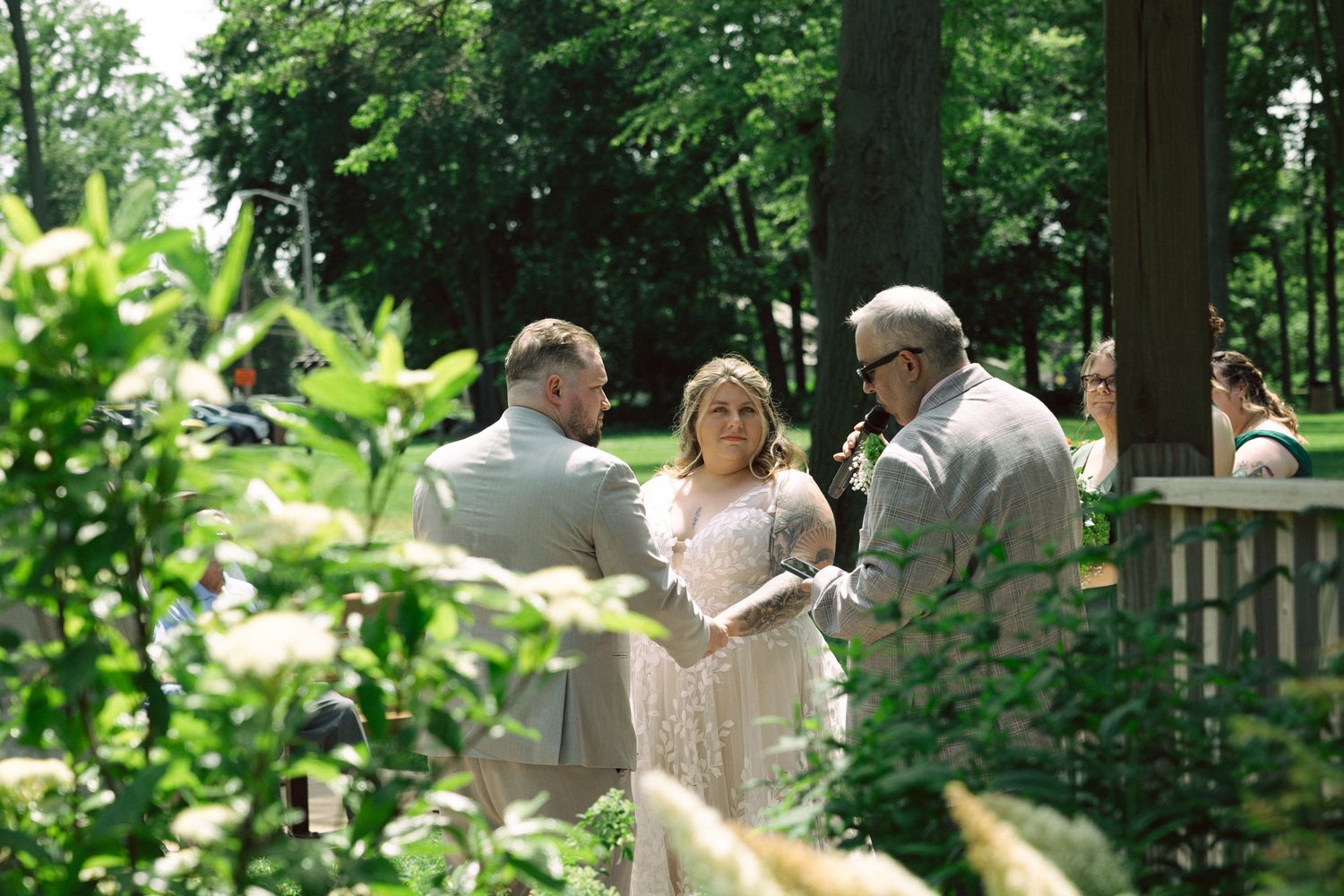 Bride and groom exchange vows outdoors in a lush garden ceremony with an officiant on a sunny day.
