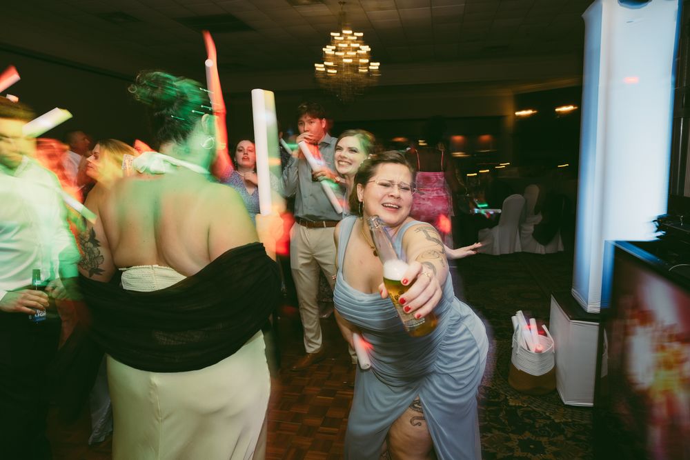 Guests dancing and celebrating at a wedding reception party in a banquet hall with colorful lights.