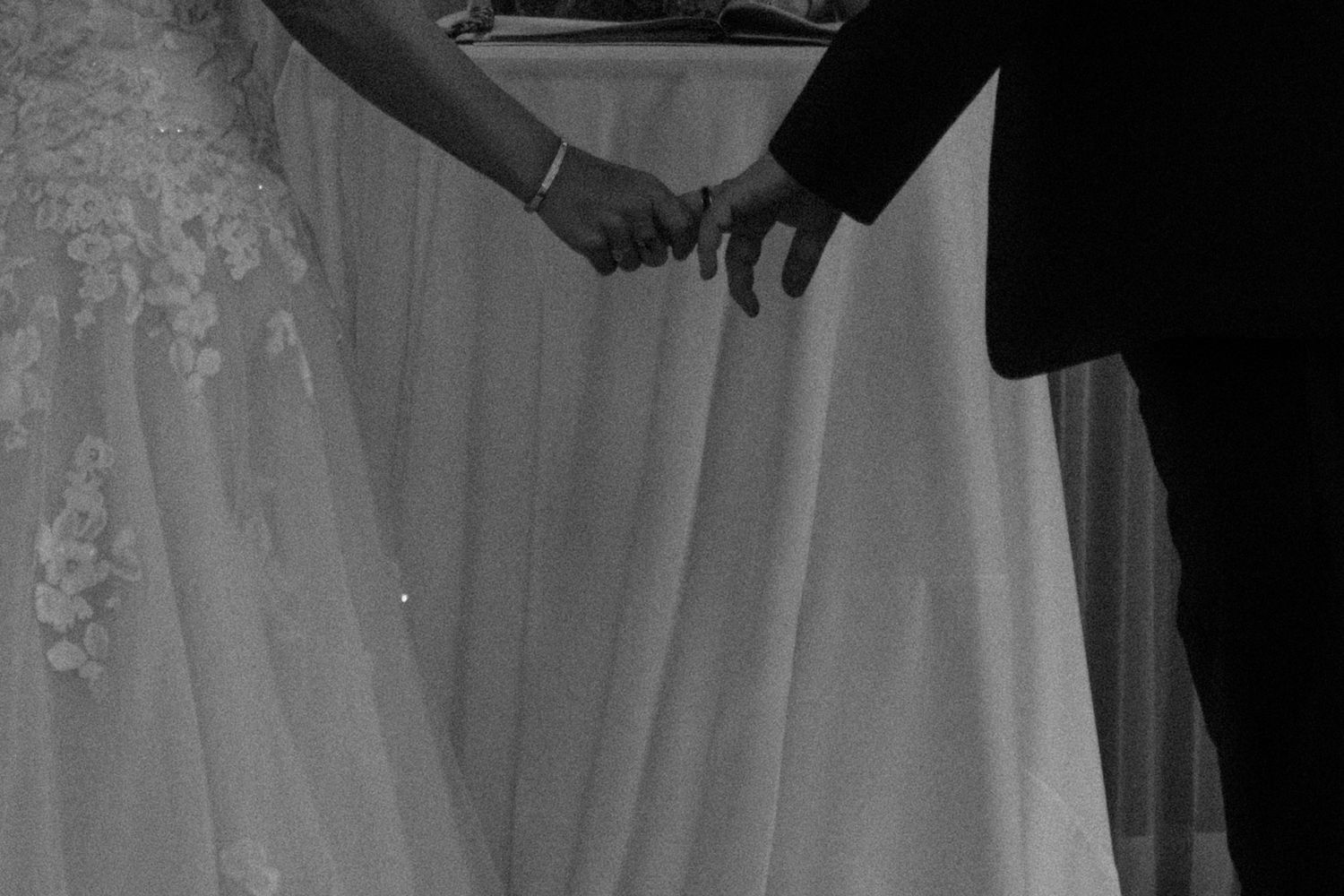 Black and white close-up of joined hands against a light fabric background.