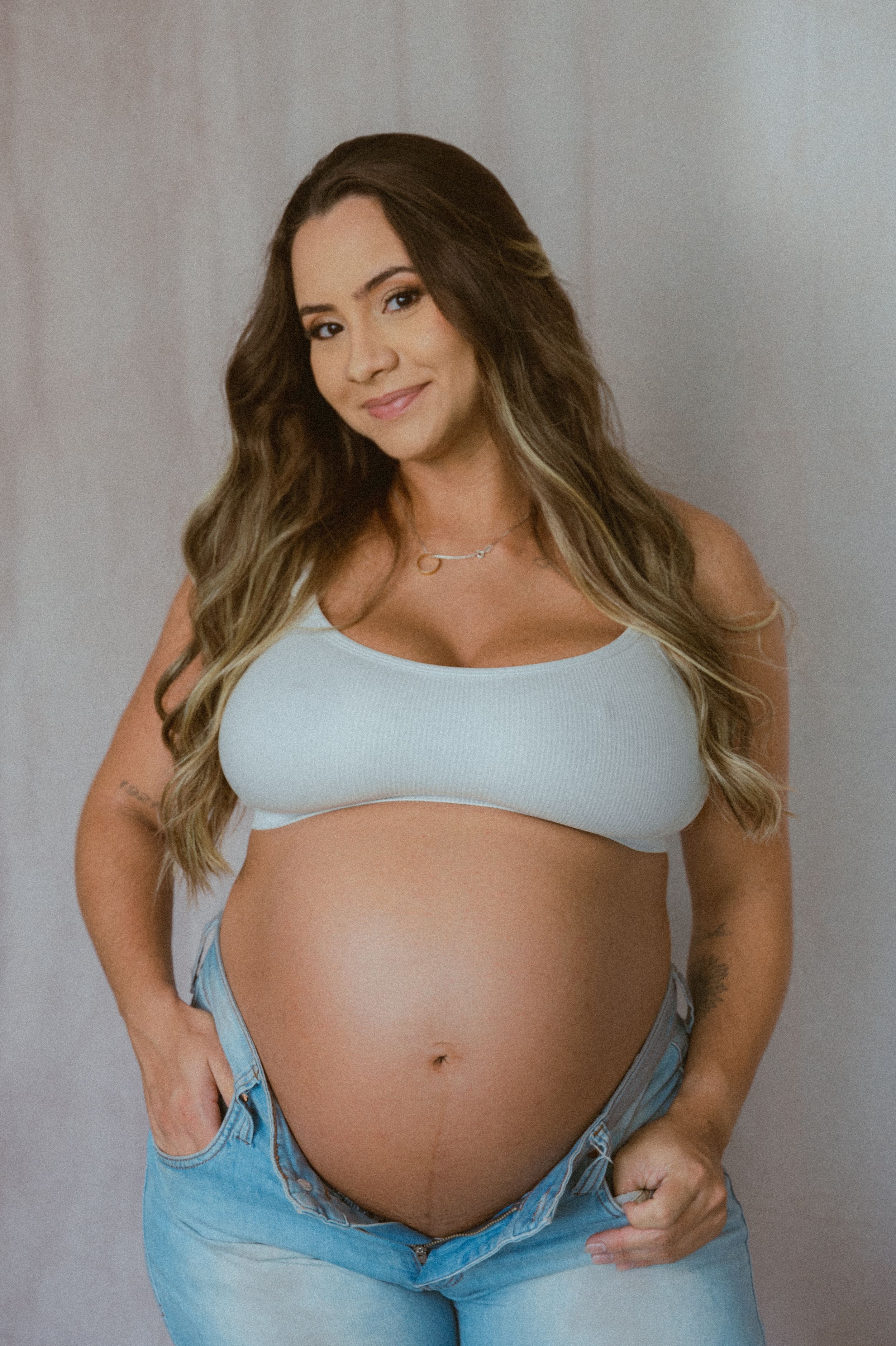 Maternity photoshoot featuring light blue crop top and growing baby bump against grey background.