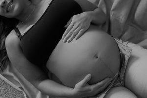 Black and white photo highlighting a pregnant belly with gentle hands cradling the bump.