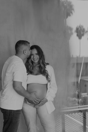 Couple in white shirts embrace during an outdoor maternity photo session.