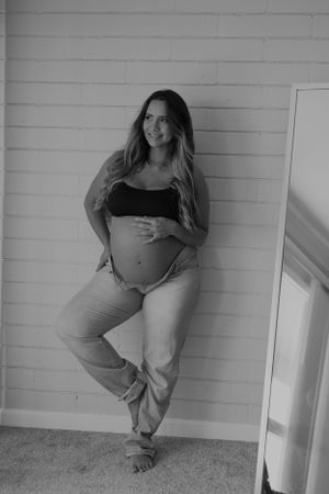 Black and white portrait of an expectant mother posing against a white wall.