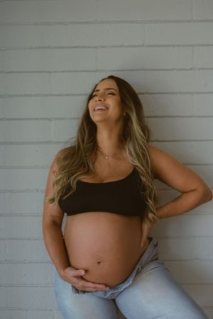 Joyful maternity photo showing a radiant pregnancy moment against white wall background.