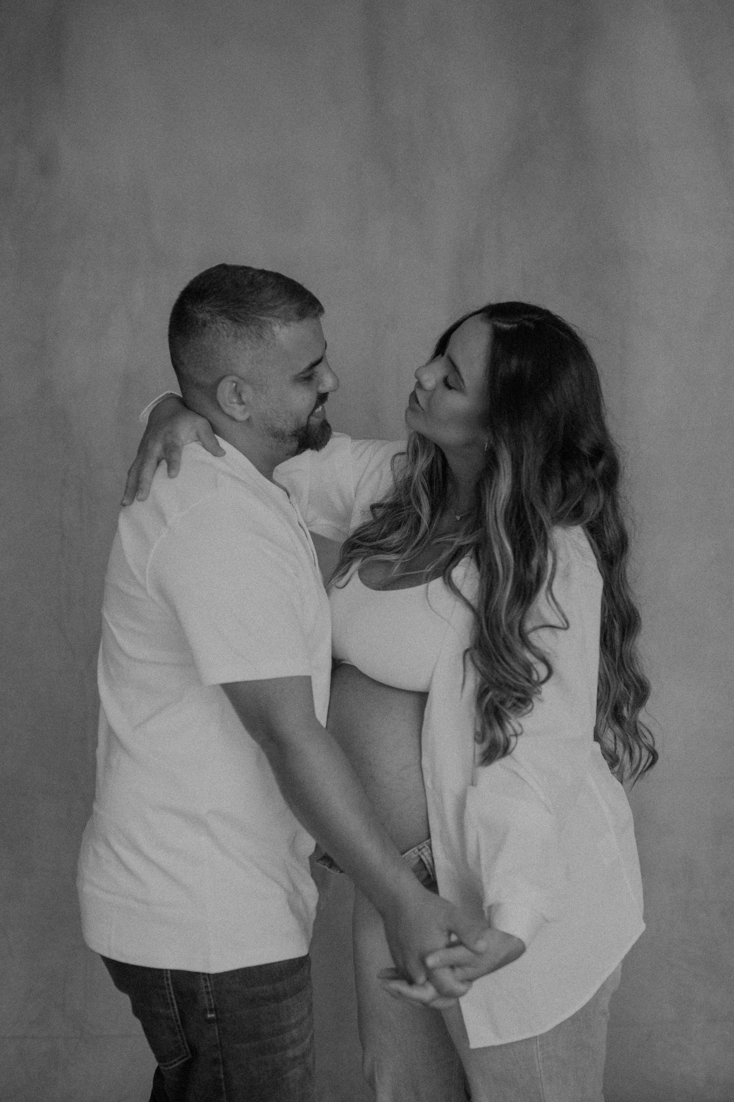 A couple in white t-shirts share tender moments during a black and white maternity photoshoot.