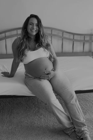 Maternity photo of an expectant mother relaxing on a bed in casual attire.