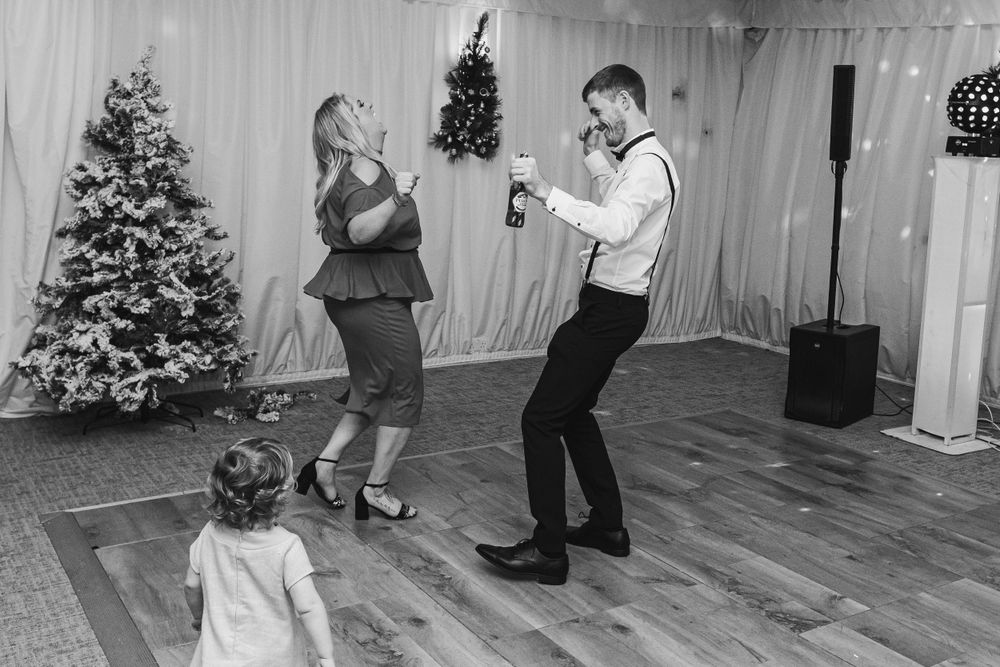 People dancing and celebrating at a wedding reception with Christmas trees and white drapes in the background.