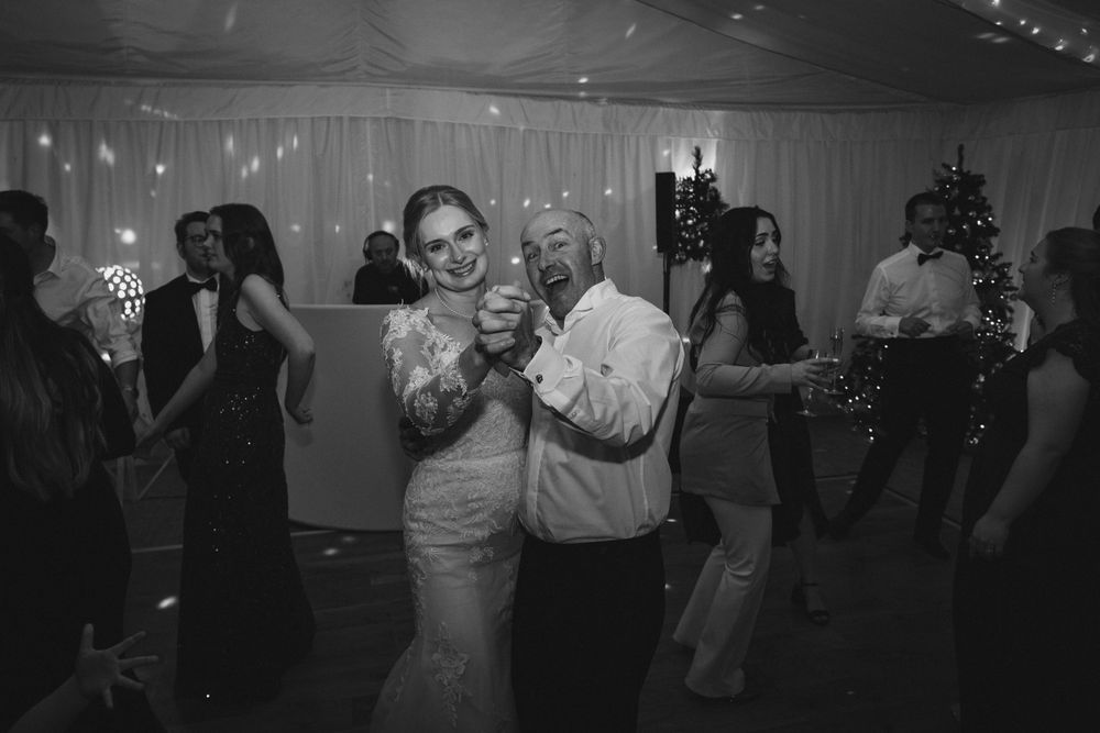 Wedding celebration with guests dancing and socializing under decorative lighting and white drapes.