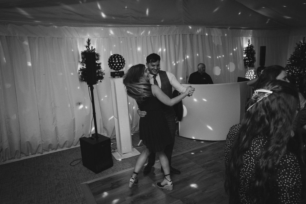 A couple dances together at a wedding reception with Christmas trees and twinkling lights in the background.