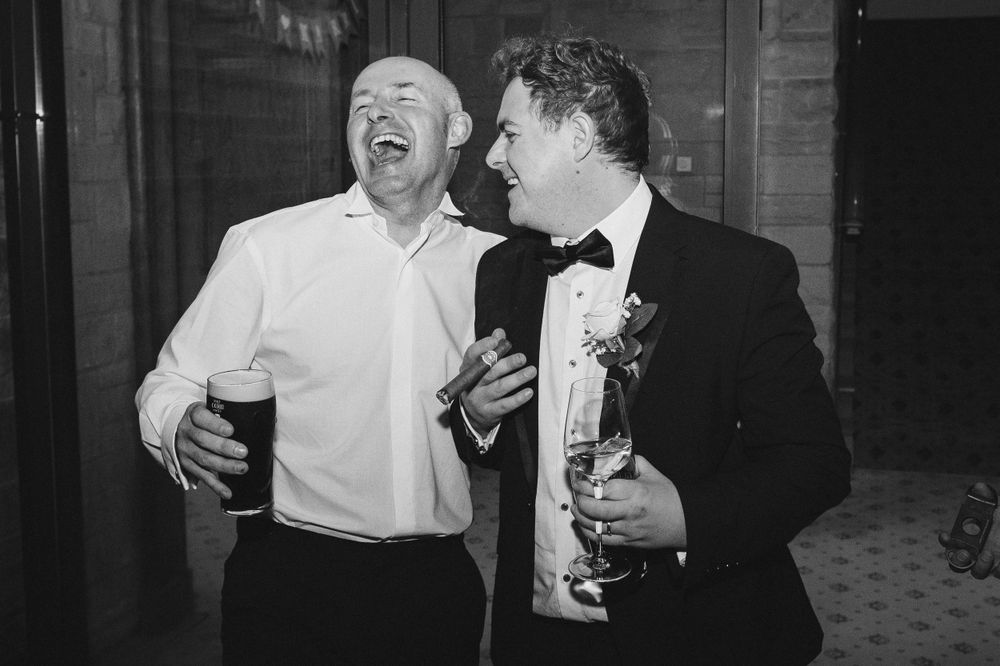 Two guests share a laugh while holding drinks at a formal event.