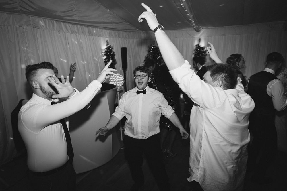 Wedding guests dancing and celebrating with drinks on the dance floor.