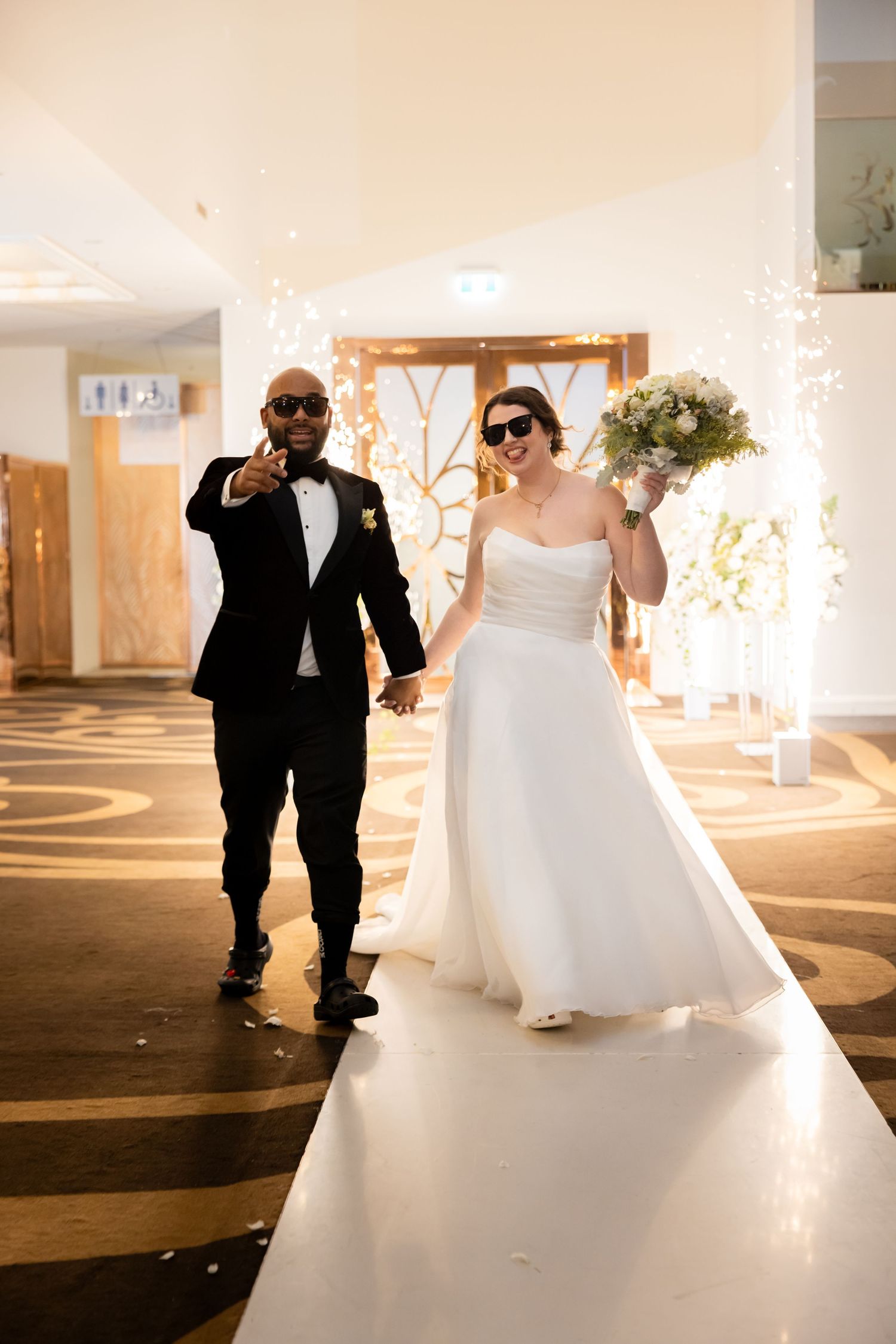 A couple walking down an illuminated white aisle at their wedding reception.