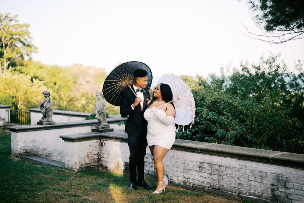 A couple holding decorative parasols poses together on stone steps in a garden setting during a romantic photoshoot.