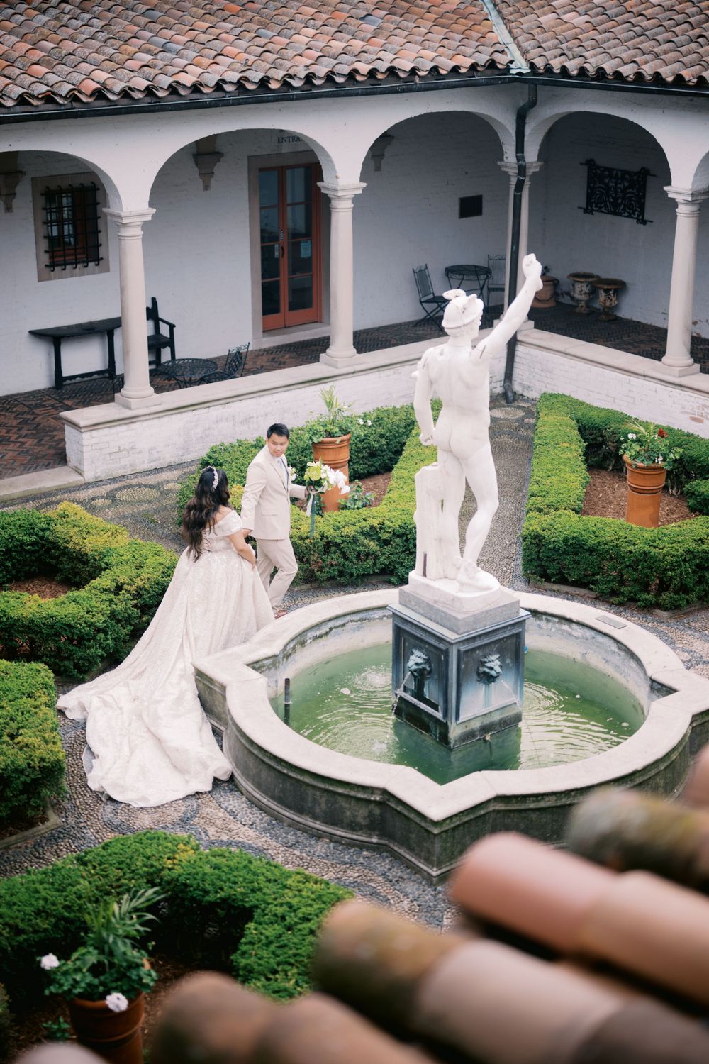 An elegant wedding scene in a Spanish colonial courtyard with arched walkways and a central fountain with white statue.
