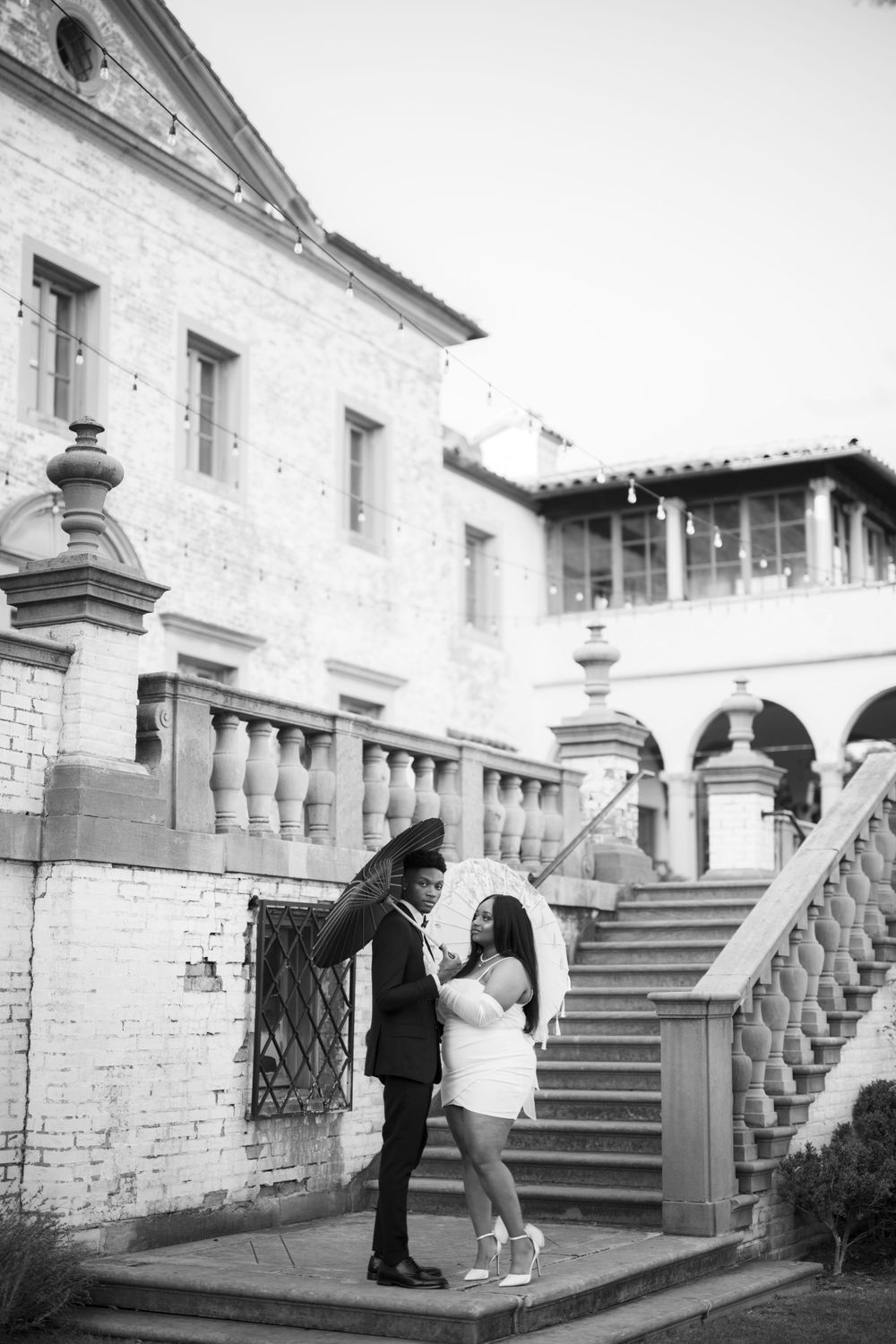A romantic couple dancing together on ornate stone steps outside a historic Spanish-style building with arches and columns.