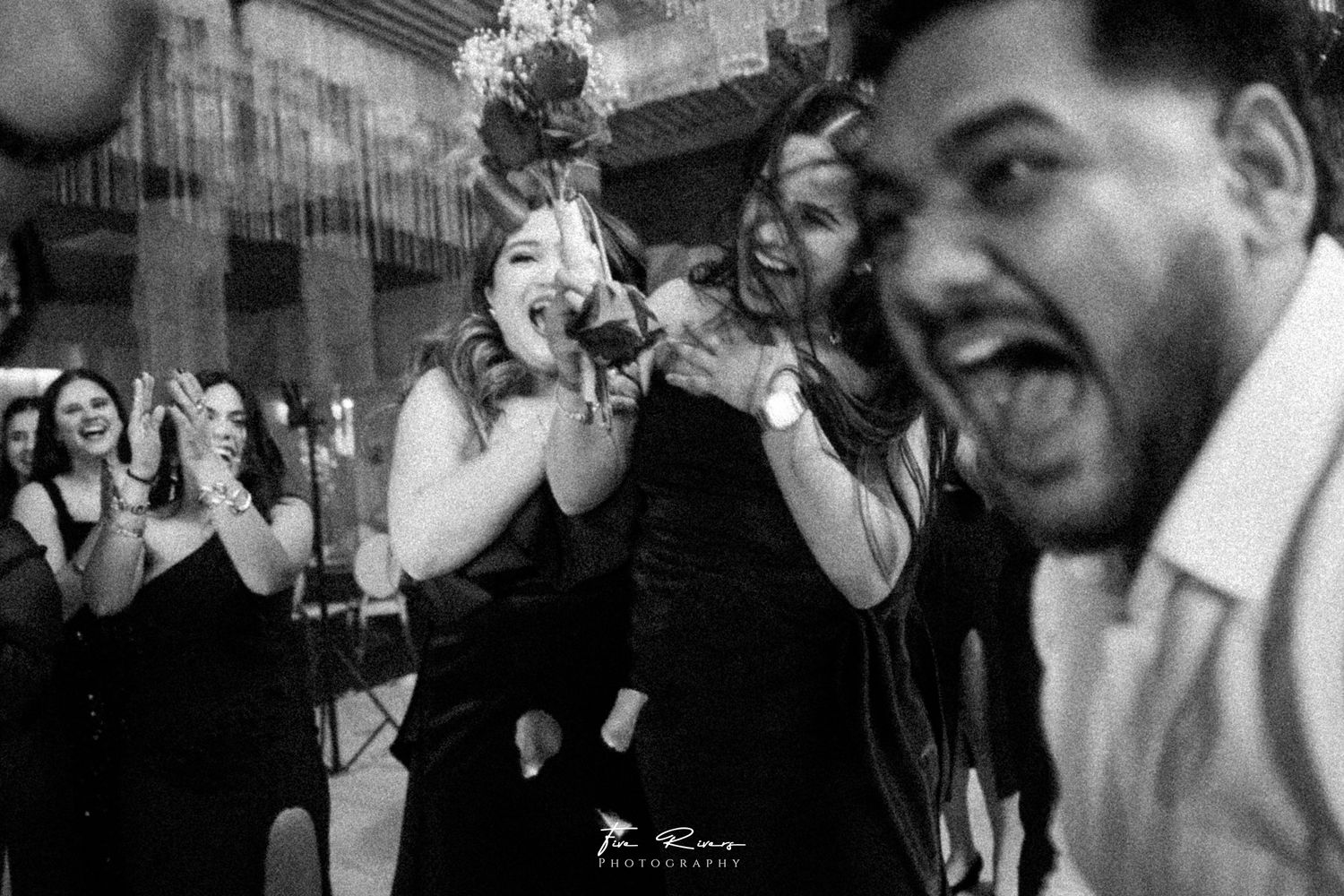 Black and white candid wedding celebration photo showing joyous emotional reactions during a celebration moment.