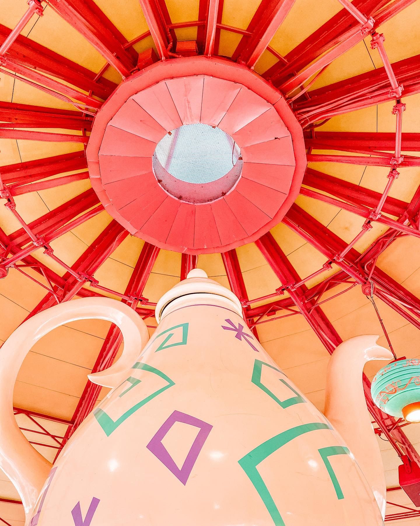 Colorful geometric paper lanterns with teal and purple patterns arranged in a radial pattern on an orange-tinted ceiling.