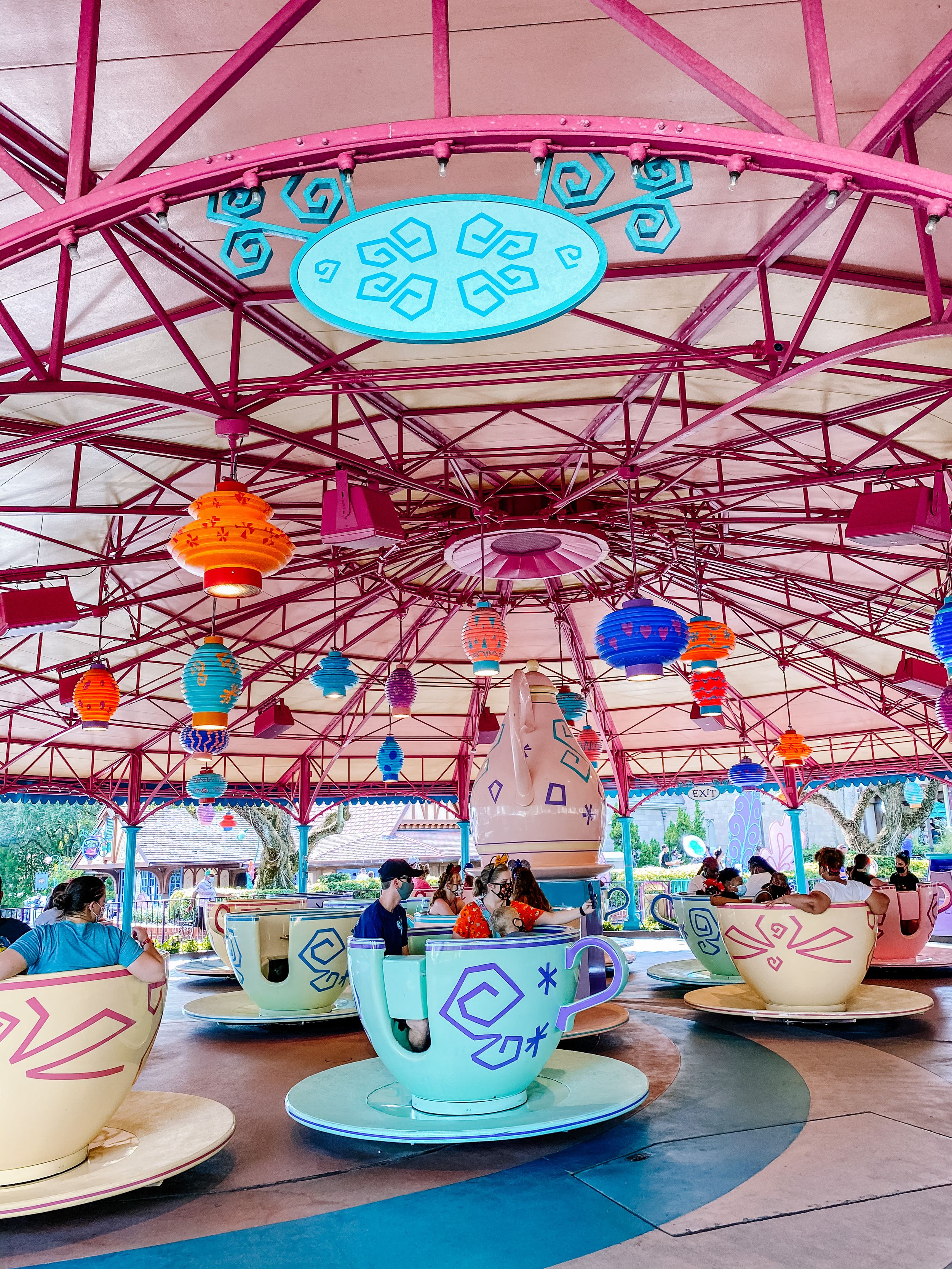 Colorful teacup ride with bright lanterns and pink metal structure at Disney's Mad Tea Party attraction.
