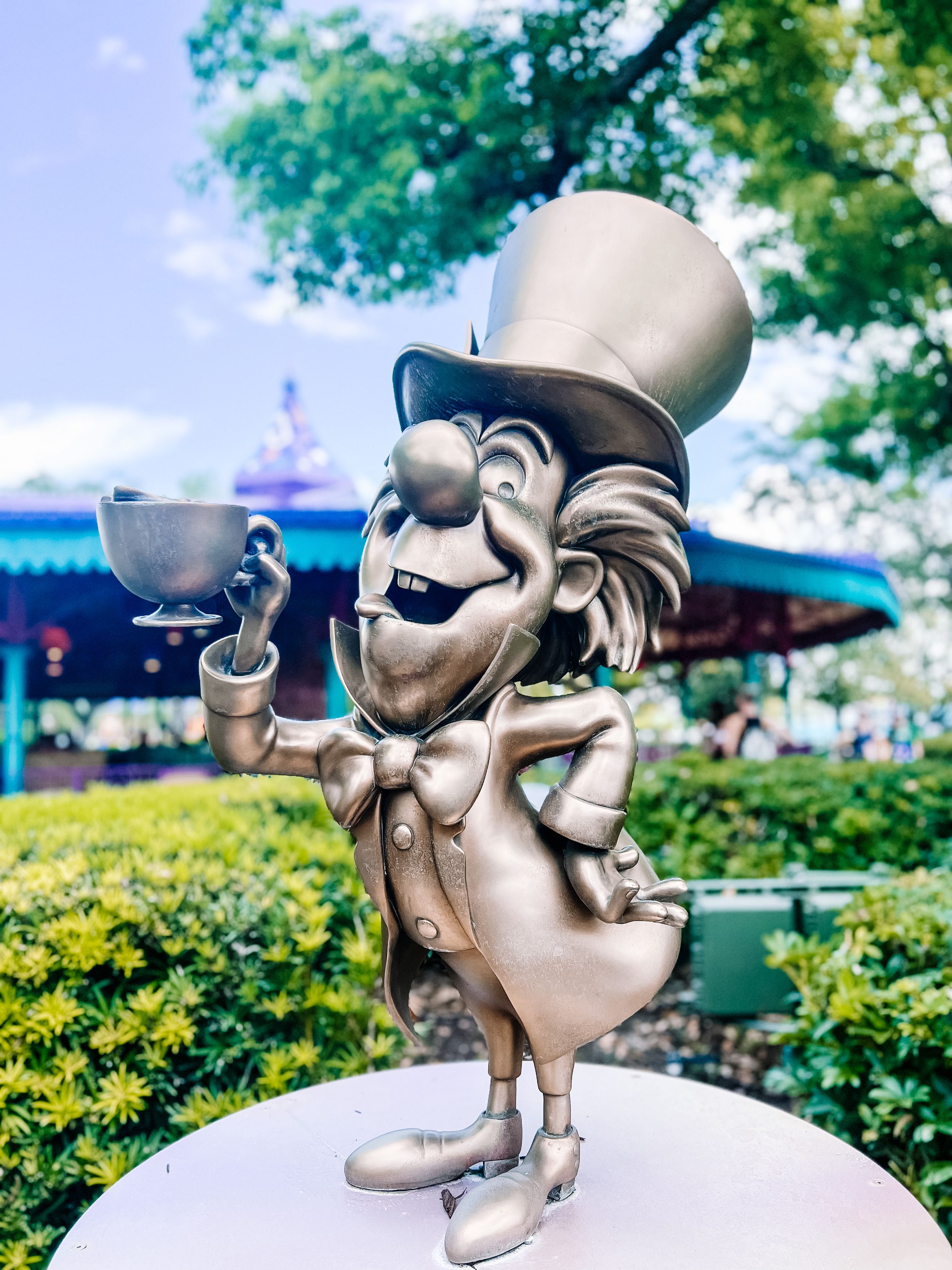 A metallic chrome sculpture of a figure smoking a long pipe shown from different angles against garden landscape backgrounds.