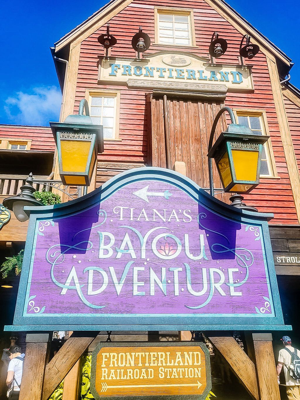 Historic Frontierland railroad station sign and Bayou Adventure signage displays at Disney theme park at sunset.
