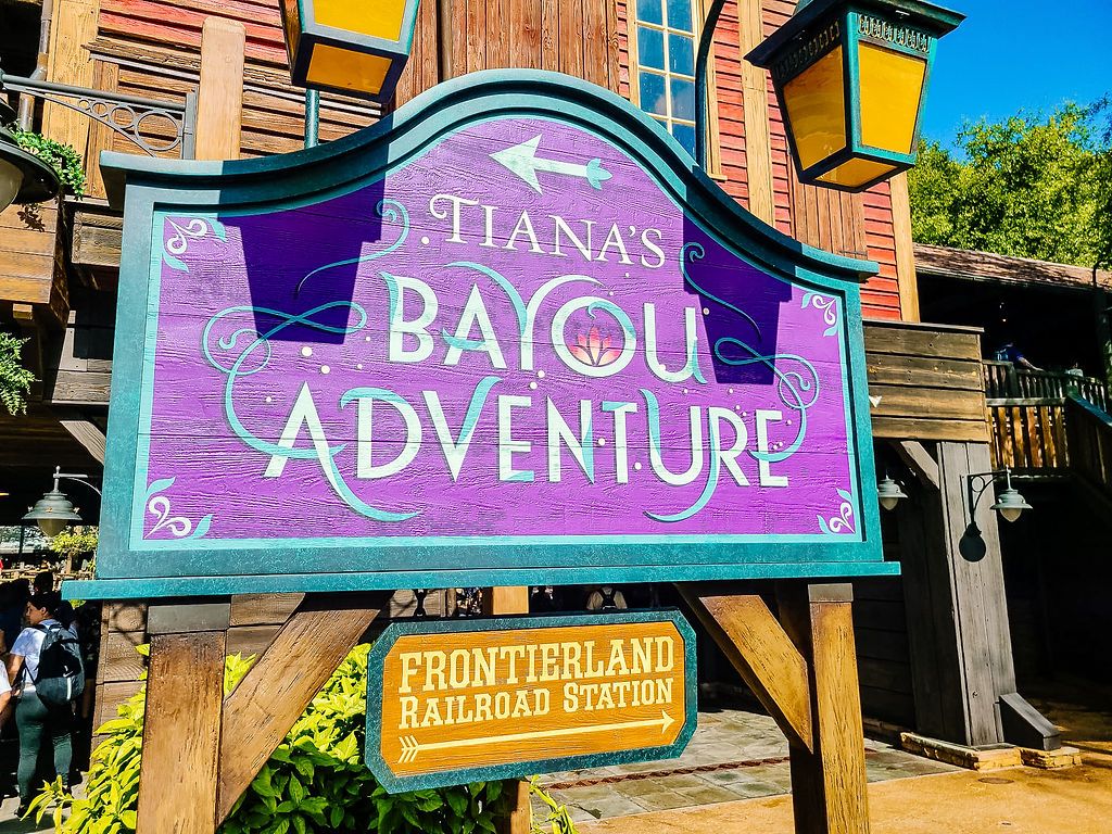 A purple sign for Tiana's Bayou Adventure attraction at Frontierland Railroad Station in Disney theme park.