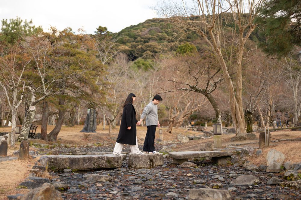 Couple facing each other on stepping stones in Japanese garden with bare winter trees and rocks.