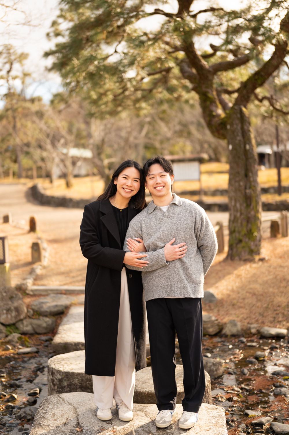 Happy couple embracing and smiling together on stone path in sunny Japanese park setting.