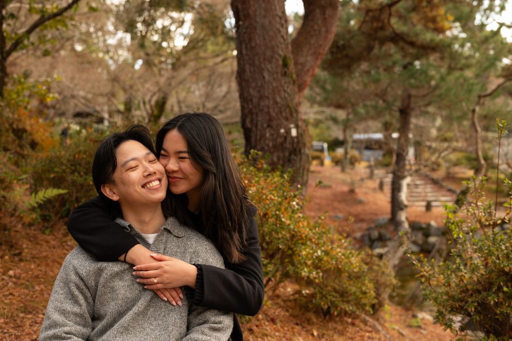 Happy couple embracing outdoors in an autumn park, woman kissing mans cheek among fall foliage.