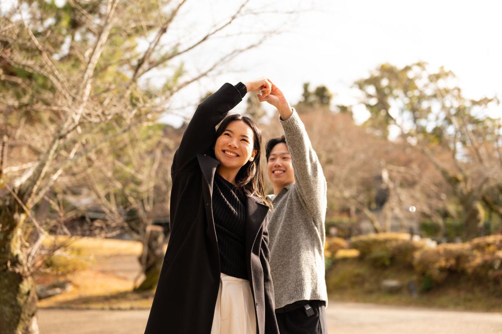 Joyful couple forming a heart shape with their arms raised in a sunlit outdoor garden setting.