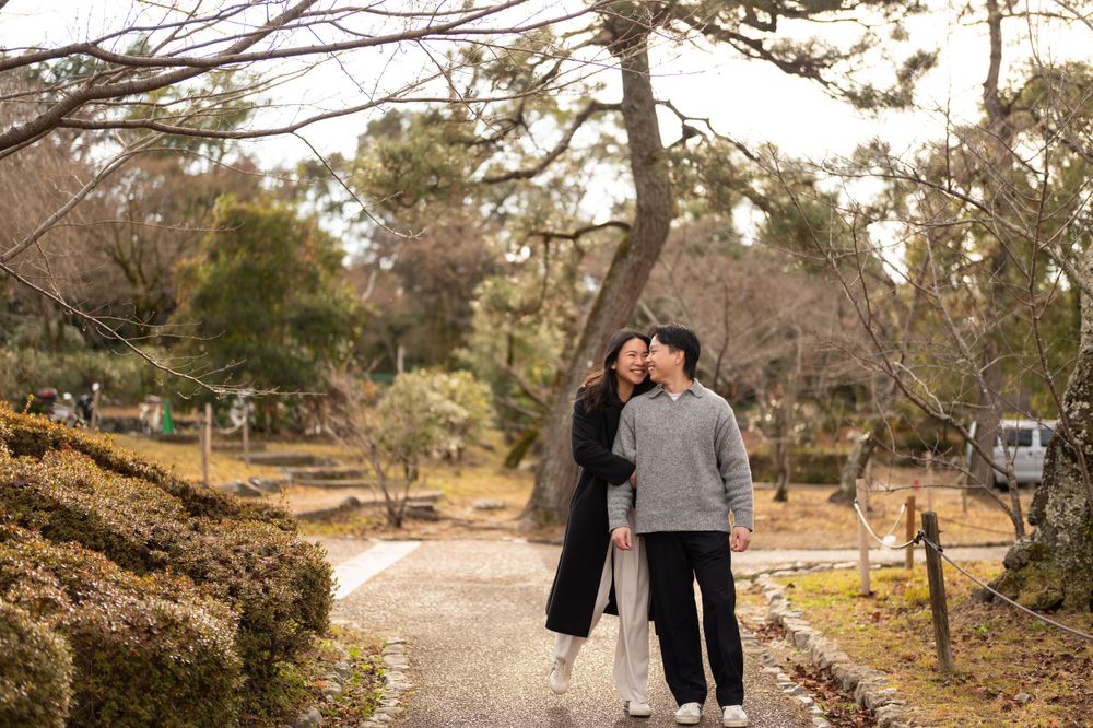 Couple embracing on a garden path surrounded by moss-covered ground and bare winter trees.