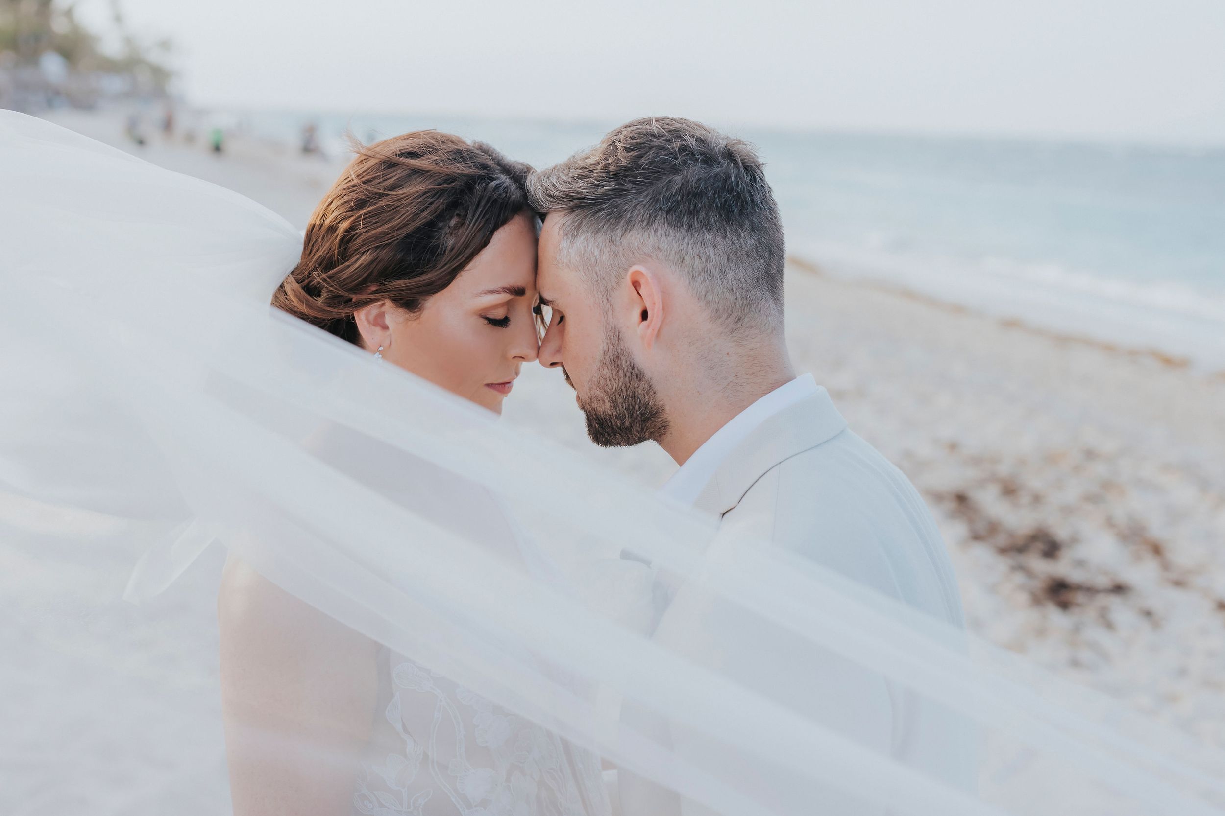 A soft, romantic beach wedding moment captured through flowing white veil.