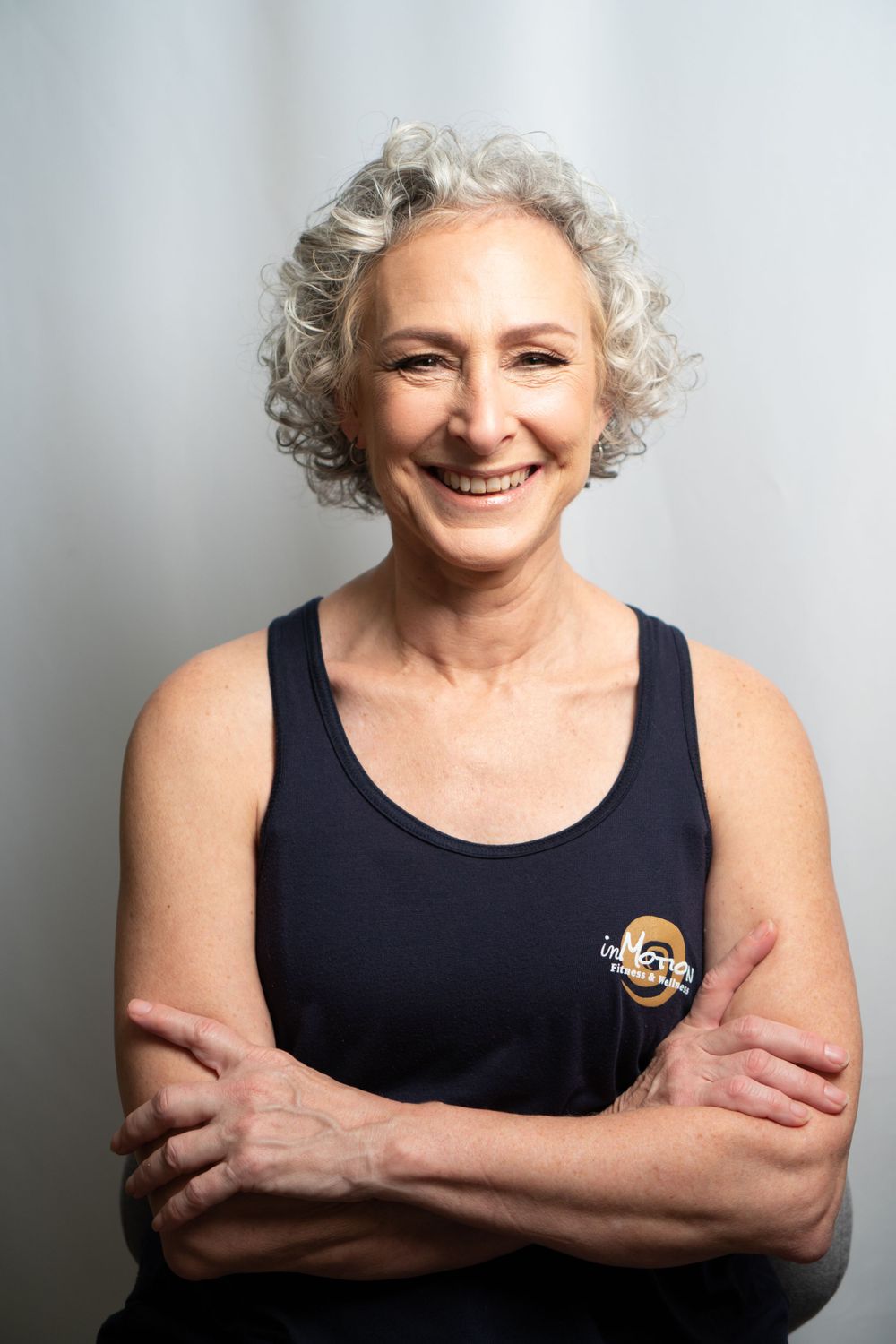 Athletic portrait of a person in a navy tank top with logo, smiling with arms crossed.