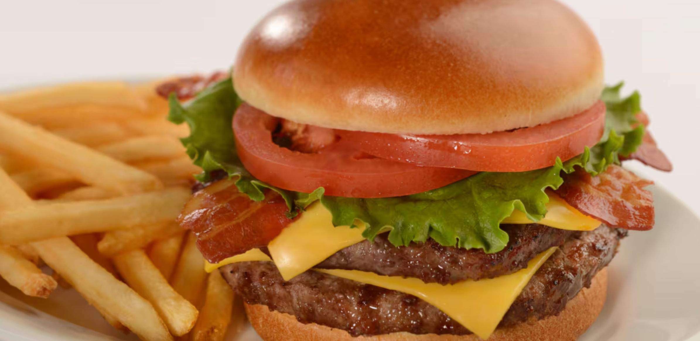 A juicy cheeseburger with lettuce, tomato, and bacon served alongside golden french fries on a plate.