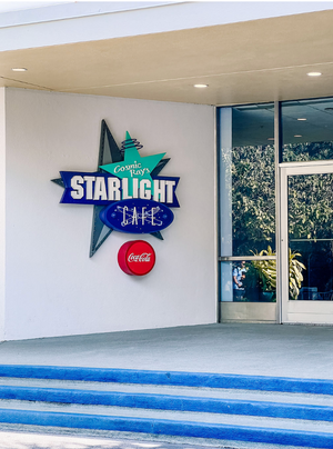 Neon Starlight diner signs with Coca-Cola branding mounted on white exterior walls of modernist building.