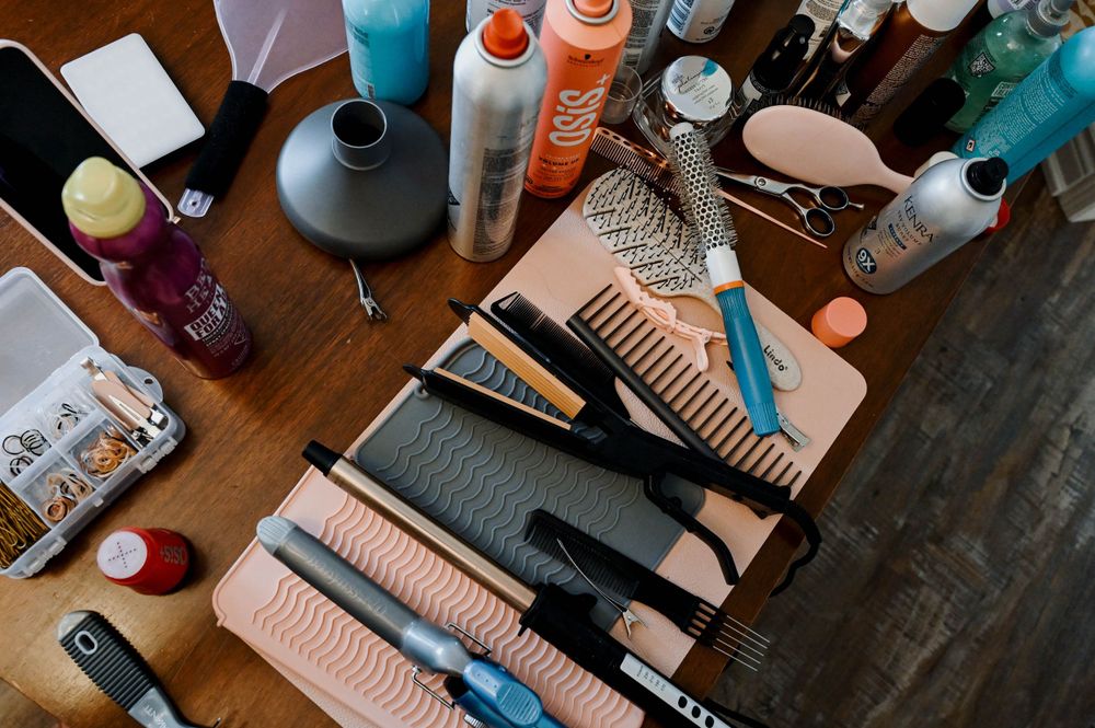 Hair styling tools and beauty products including combs, clippers, sprays and styling accessories arranged on dark wooden surface.