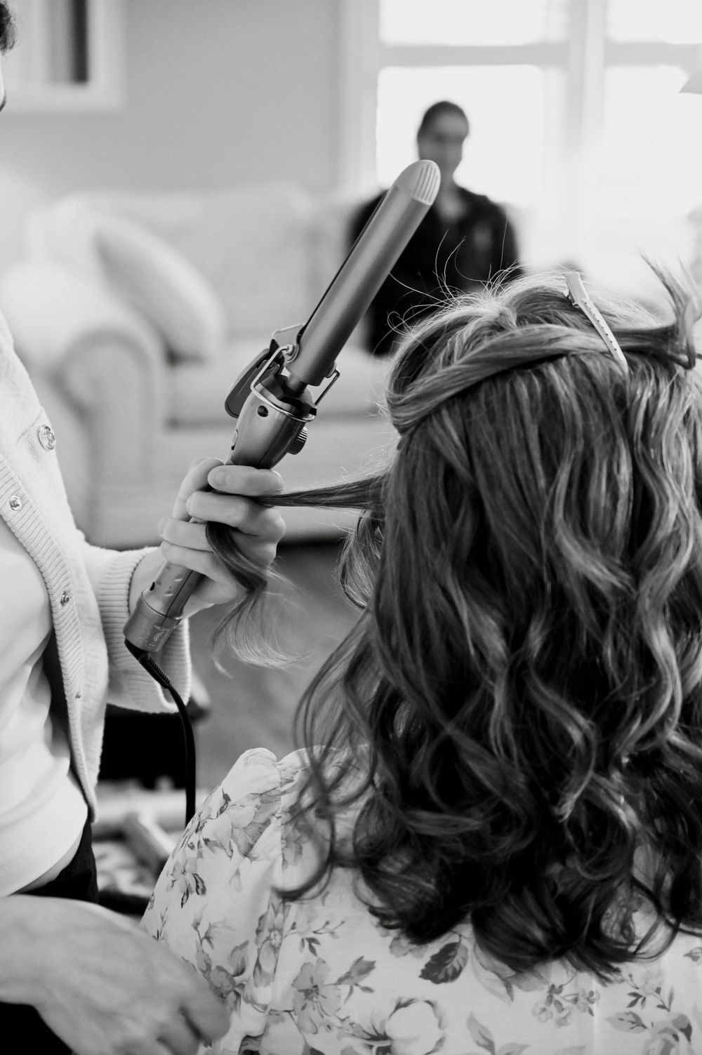 Black and white photo of a hairstylist using a curling iron on long wavy hair during a styling session.