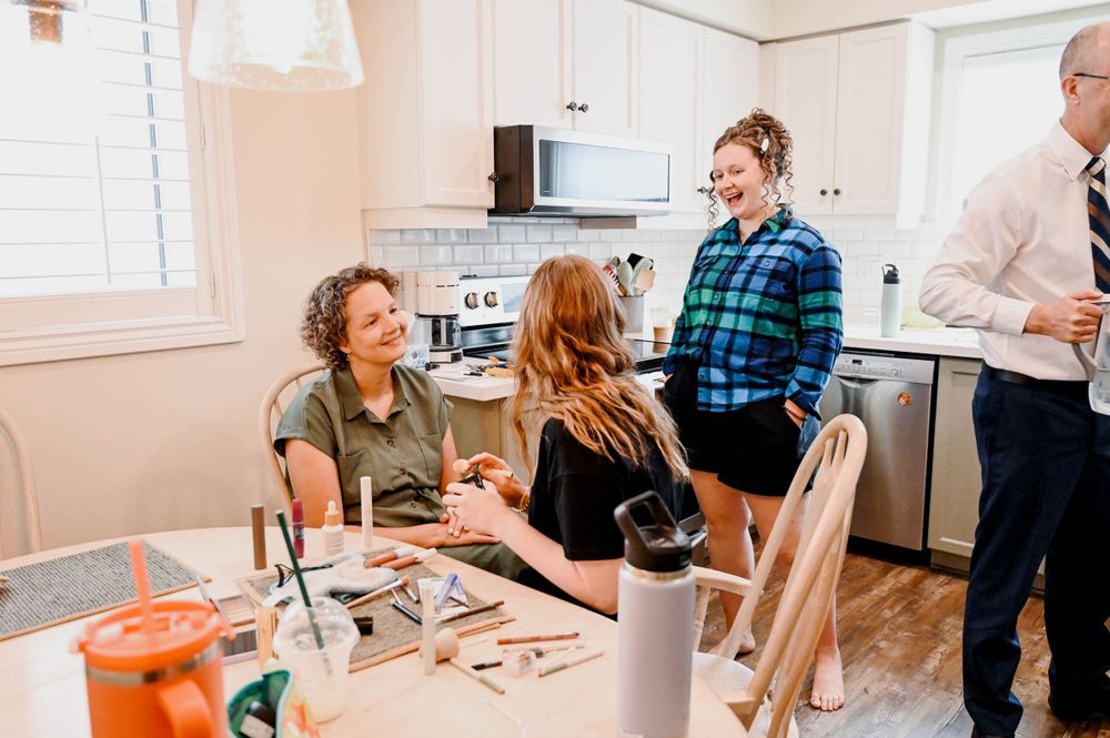 Group gathers in bright modern kitchen for casual conversation around wooden dining table.