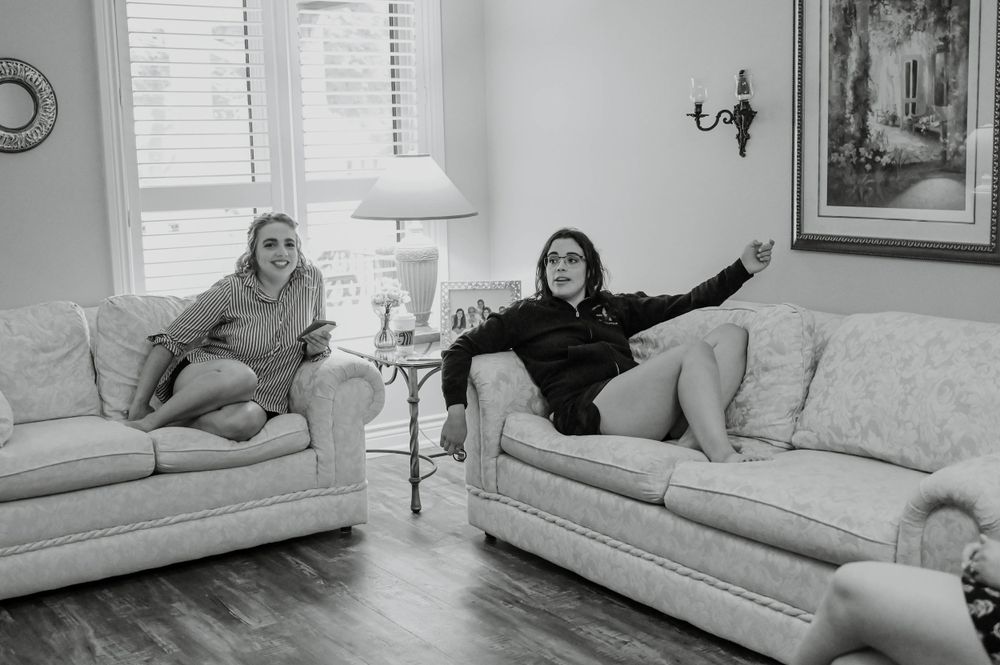 Two people lounging casually on matching floral sofas in a living room with hardwood floors and white walls.