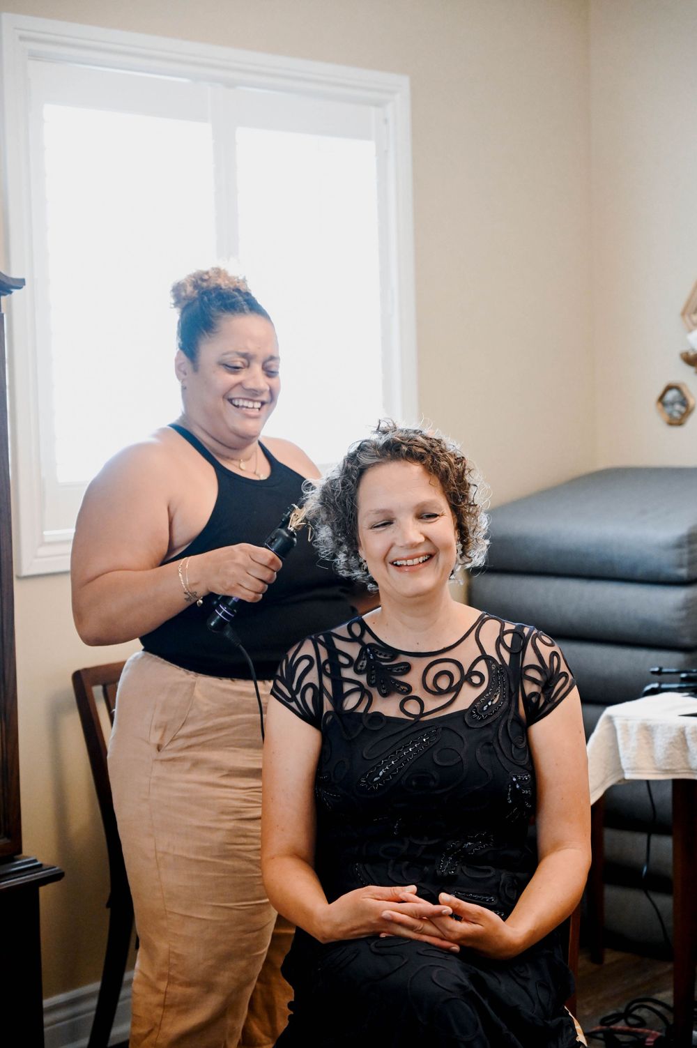 Two people share a cheerful moment during a styling session in a room with white decor.