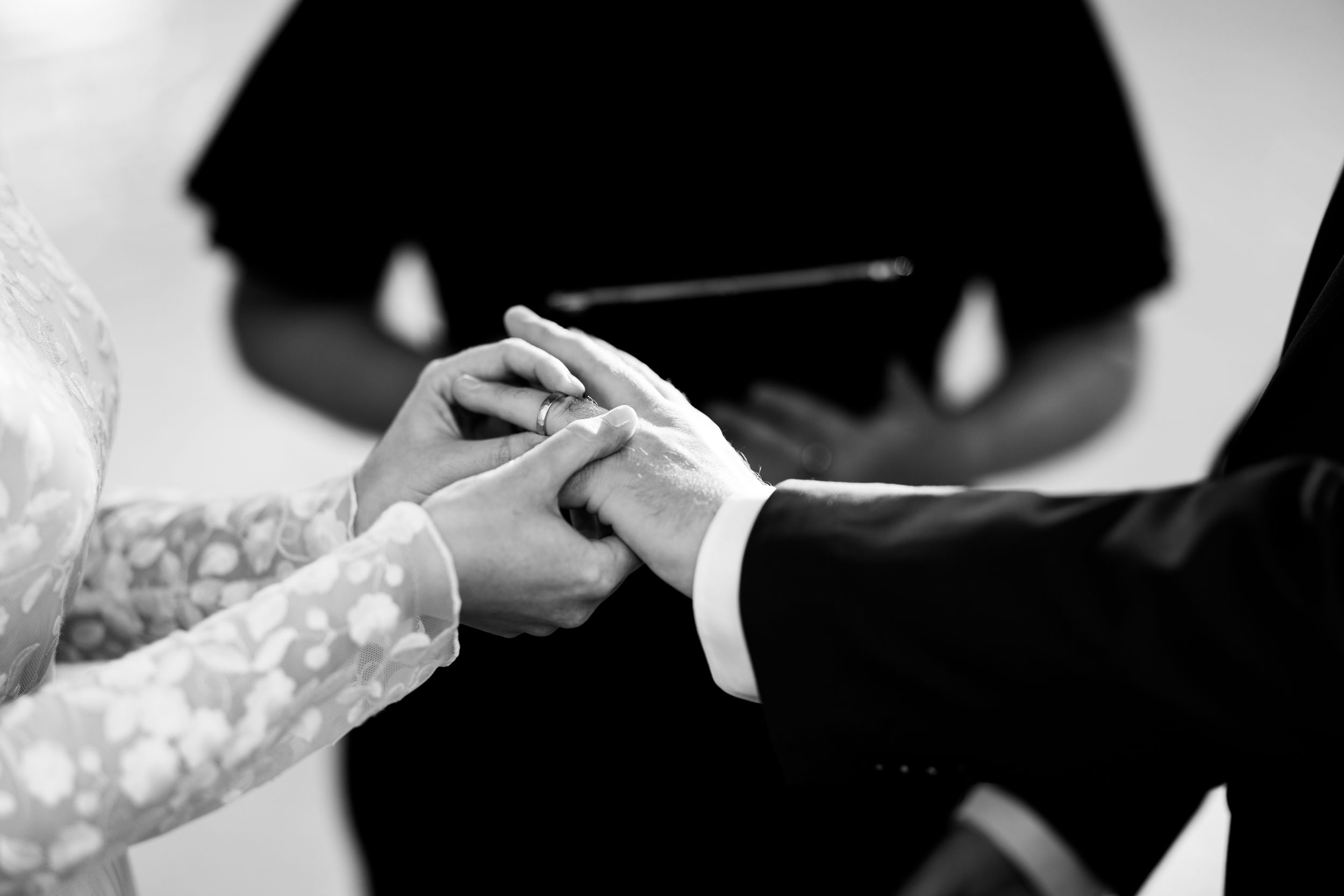 A black and white close-up of hands exchanging wedding rings during a ceremony.