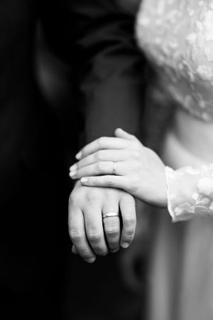 A black and white close-up of newlywed hands showing wedding rings.